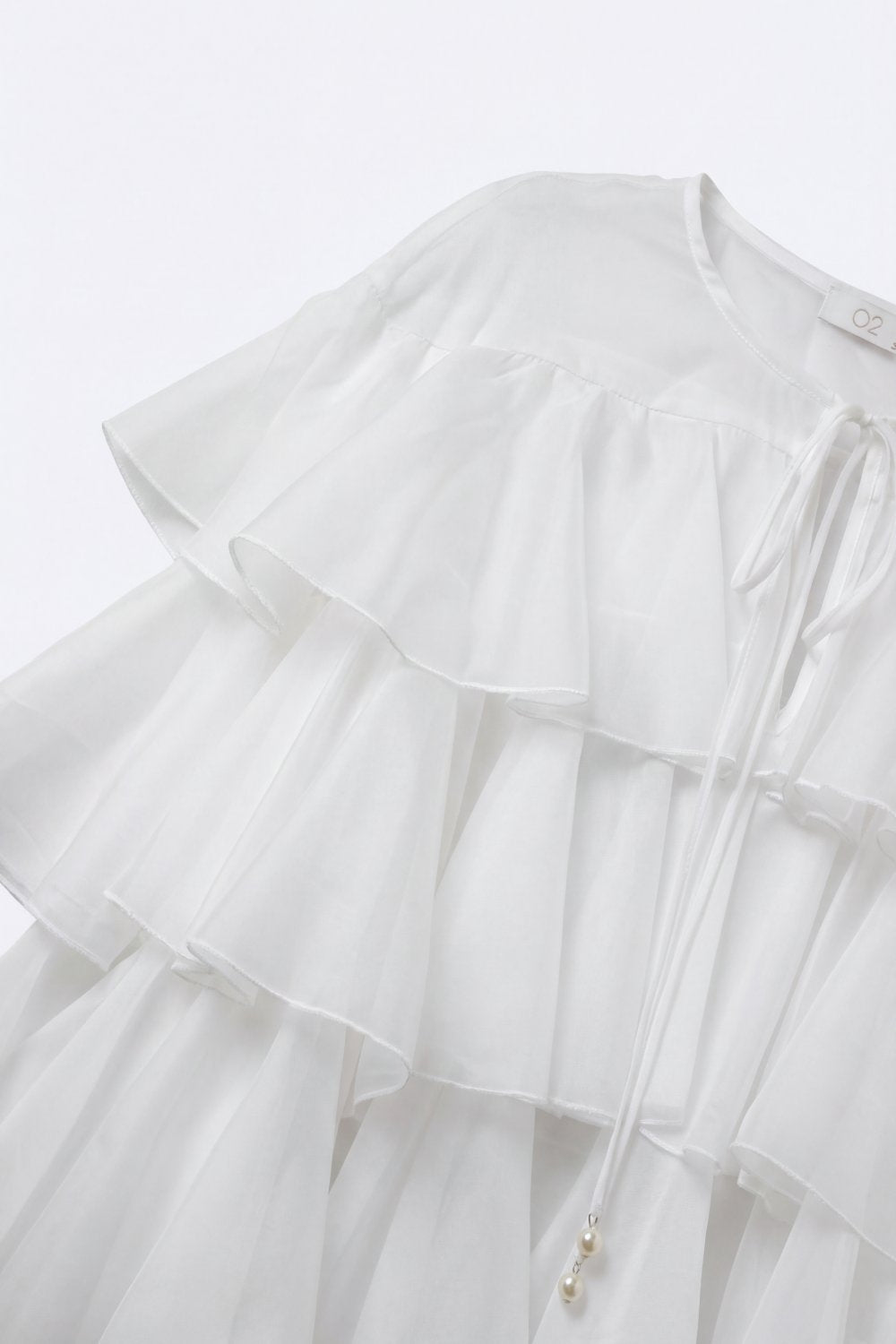 Blusa bianca con volant a strati e peplo con fiocco al collo